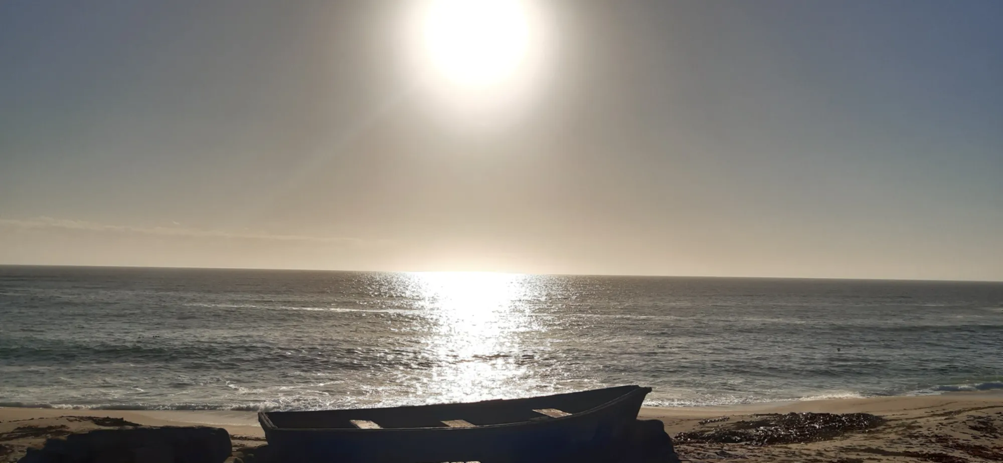 Die Sonne steht tief über dem Meer, eine Bank am Strand